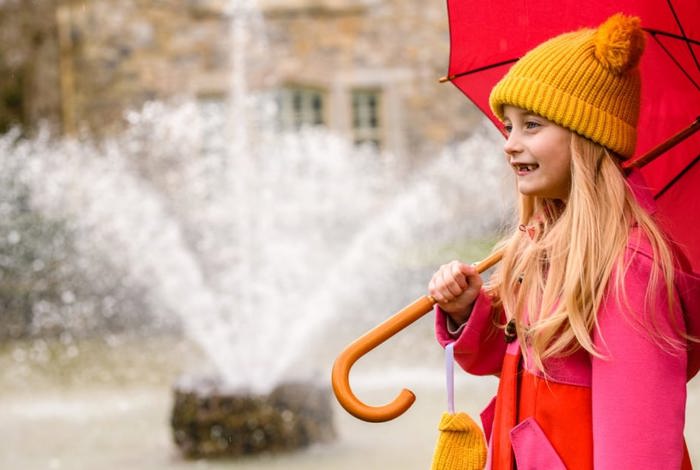 Child with pink umbrella smiling in the rain