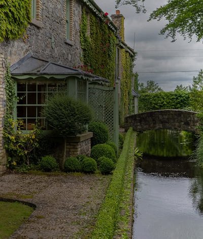 External view of Irish hotel with canal and stone cottage building